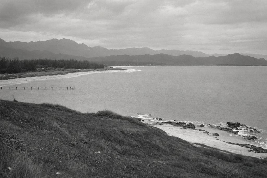 Historic view of Kailua Beach, Oahu, showing remnants of an early pier or landing, an undeveloped shoreline, and the Koolau Mountains in the background.