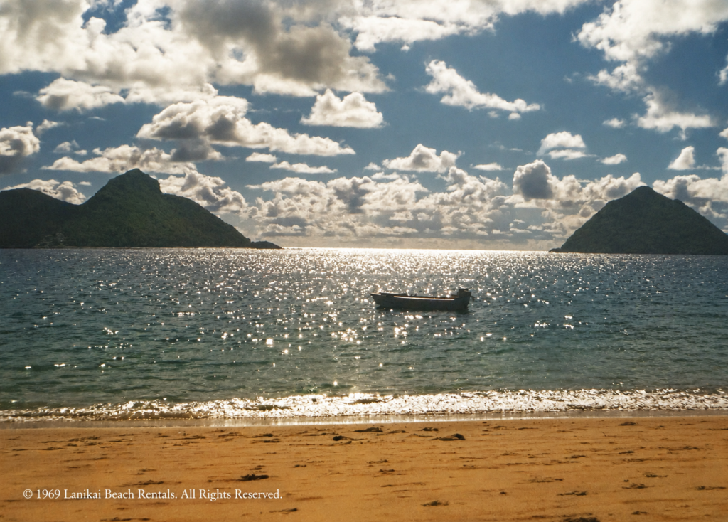 Historic family photograph of Lanikai Beach, Oahu, showing the sandy shoreline, sparkling ocean, small boat, and Mokulua Islands offshore.