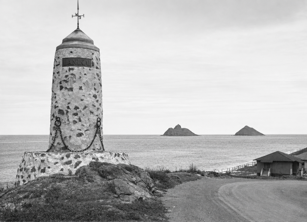 Historic 1925 photograph of the Lanikai Monument at Alala Point, Oahu, with the Mokulua Islands offshore and early Lanikai development nearby.