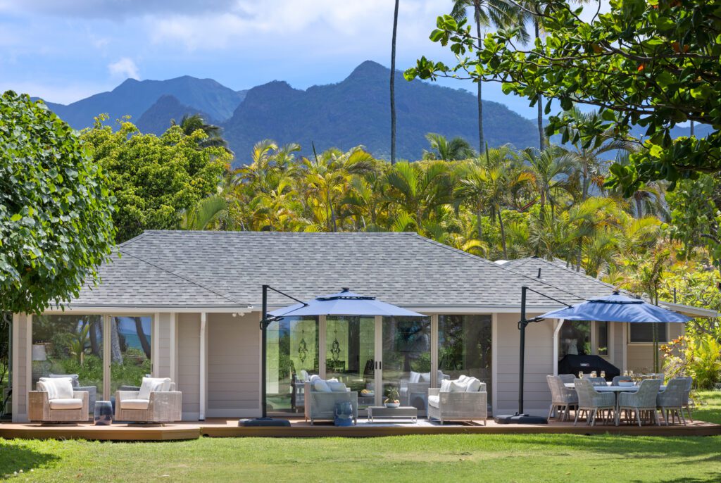 Main house with navy market umbrellas and outdoor lounge beneath the Koʻolau Mountains at Kailuana Beachfront Estate