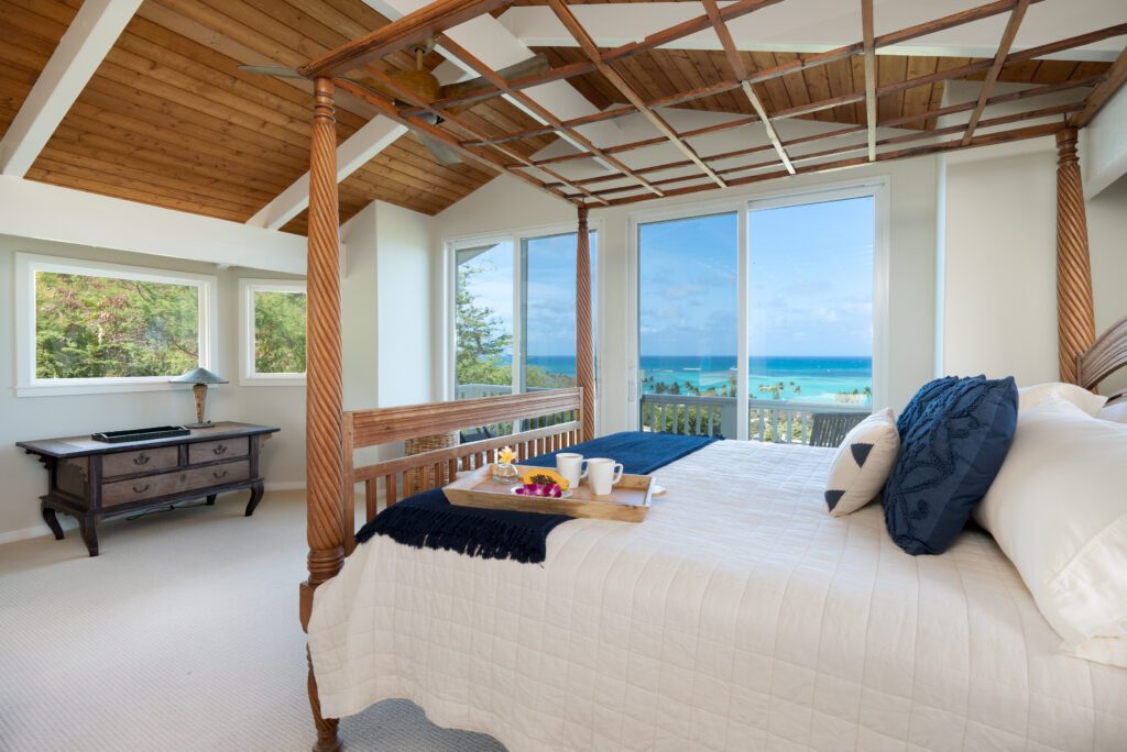 Primary suite with four-post king bed and ocean view at Makani Moana