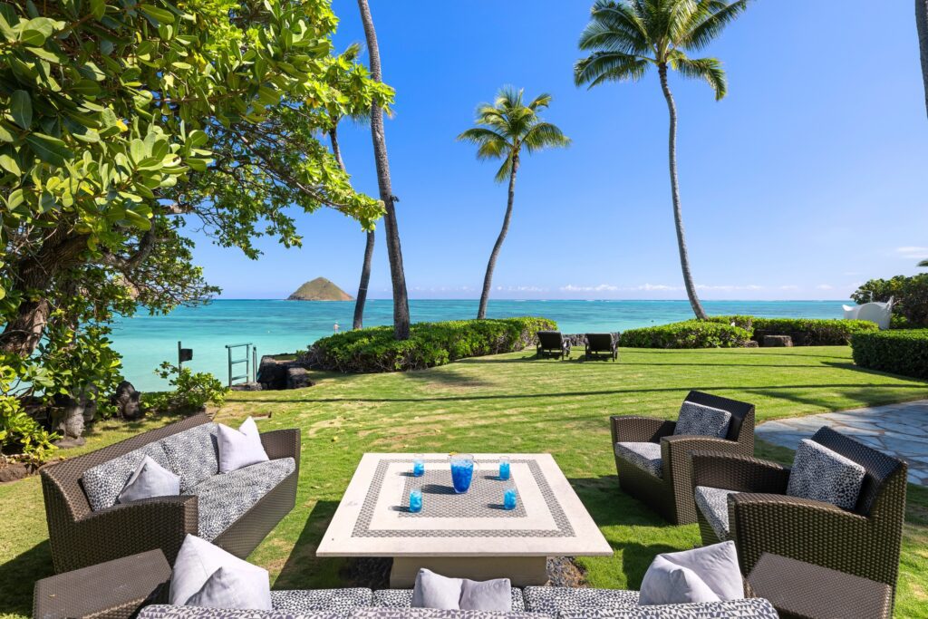 Outdoor lounge with wicker sofas and a stone coffee table on the oceanfront lawn at Paul Mitchell Estate