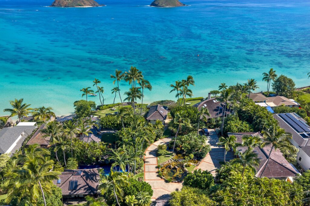 Aerial view over the estate's palms and roofs toward turquoise water and the Mokulua Islands at Paul Mitchell Estate