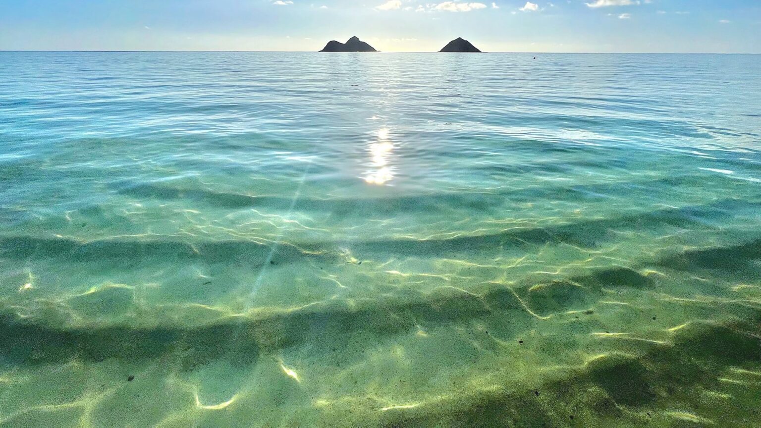 The Mokulua Islands on the horizon beyond the clear turquoise water of Lanikai Beach